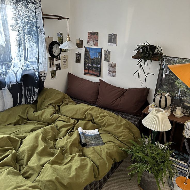 an unmade bed in a room with pictures on the wall and plants next to it