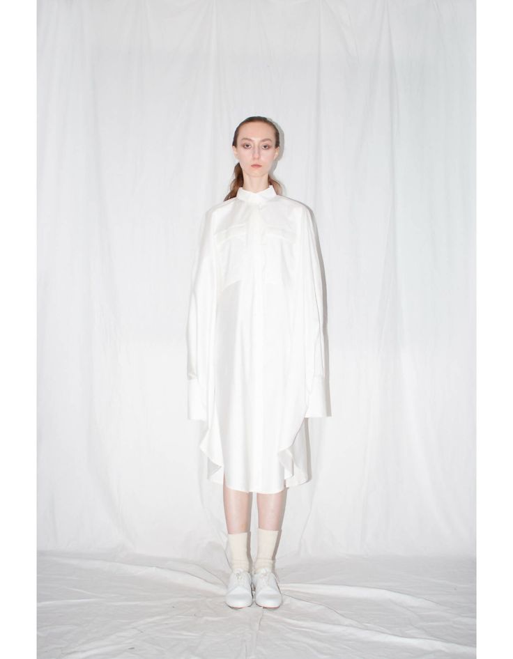 White zero waste cloak shirt is bias-cut that ensures a voluminous silhouette and flattering fit. Constructed from 100% Italian cotton, the shirt features slim cut collar, front covered placket button closure, 2 patch pockets, buttoned side seam vents and elongated one button sleeve cuffs.FEATURES:- Cloak shirt- 100% Italian cotton- Zero waste product- Side seam slits with buttons- Slim collar- Concealed front placket button closure- Bias cut- Styled here with our White Artisanal Shoes- Entirely Spring Shirt With Concealed Placket And Shirttail Hem, Fall Shirt With Concealed Placket For Daywear, Oversized White Shirt Dress For Fall, Modern Fall Shirt For Daywear, Fall Daywear Tops With Concealed Placket, Spring Long Sleeve Shirt With Concealed Placket, White Blouse With Concealed Placket For Spring, White Shirt With Asymmetrical Hem For Work, White Workwear Shirt With Asymmetrical Hem