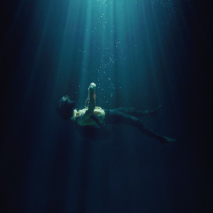 a man is swimming in the water with his hand up to his head while holding an object