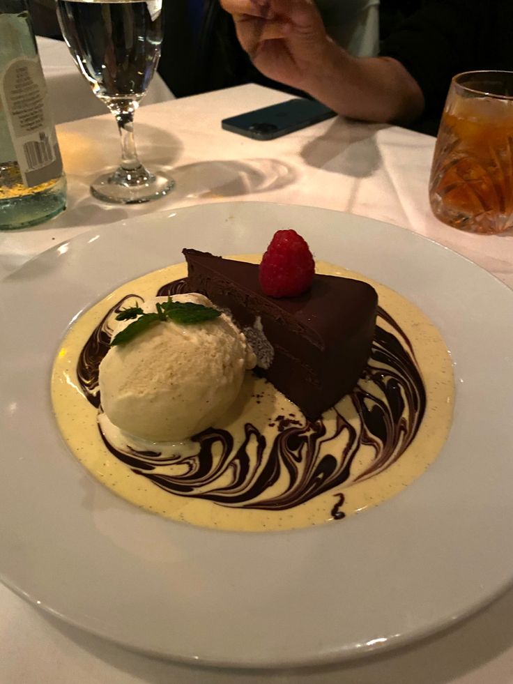 a white plate topped with a piece of cake and ice cream next to a glass of wine