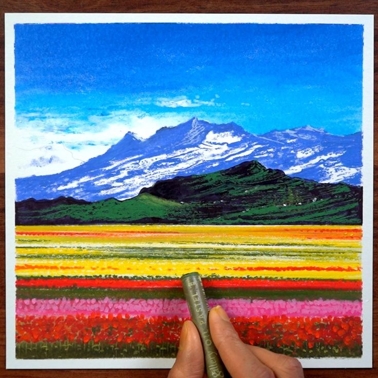 a hand holding a pencil in front of a painting with mountains and flowers on it