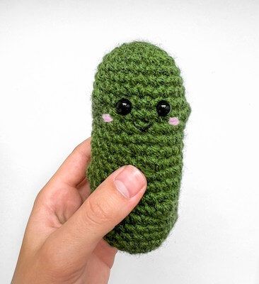 a hand holding a green crocheted object with eyes on it's face