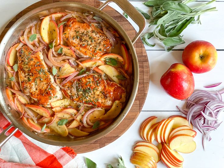 a pan filled with meat and onions next to sliced apples on a white wooden table