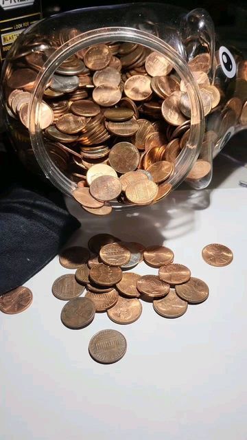 a jar filled with lots of coins sitting on top of a white table next to a pair of black pants