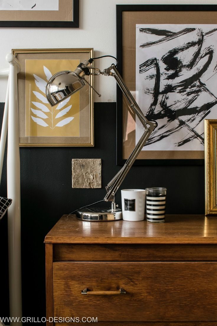 a desk lamp sitting on top of a wooden dresser next to pictures and paintings above it