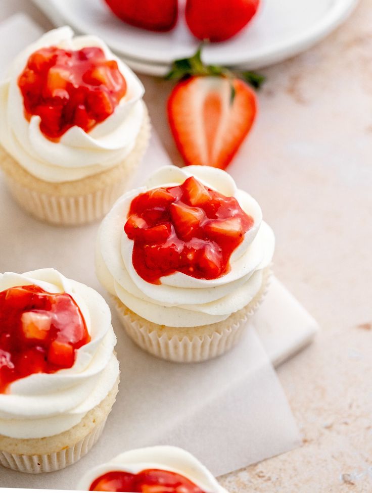 three cupcakes with white frosting and strawberries