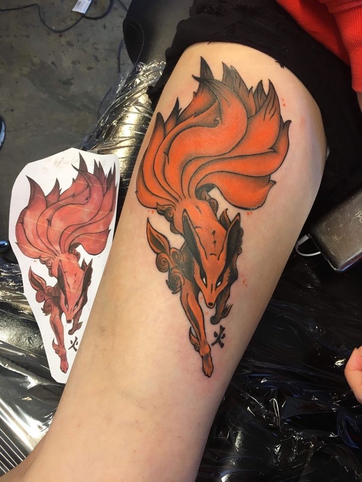 an orange and black tattoo on the leg of a woman's arm with two foxes