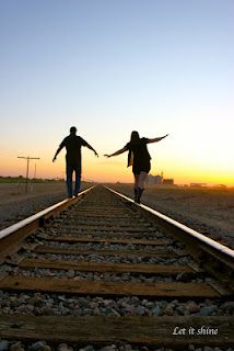 two people walking on train tracks with their arms outstretched in front of the sun setting