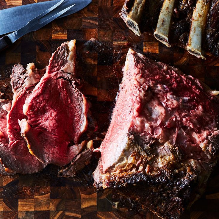 two pieces of meat on a cutting board next to knifes and utensils