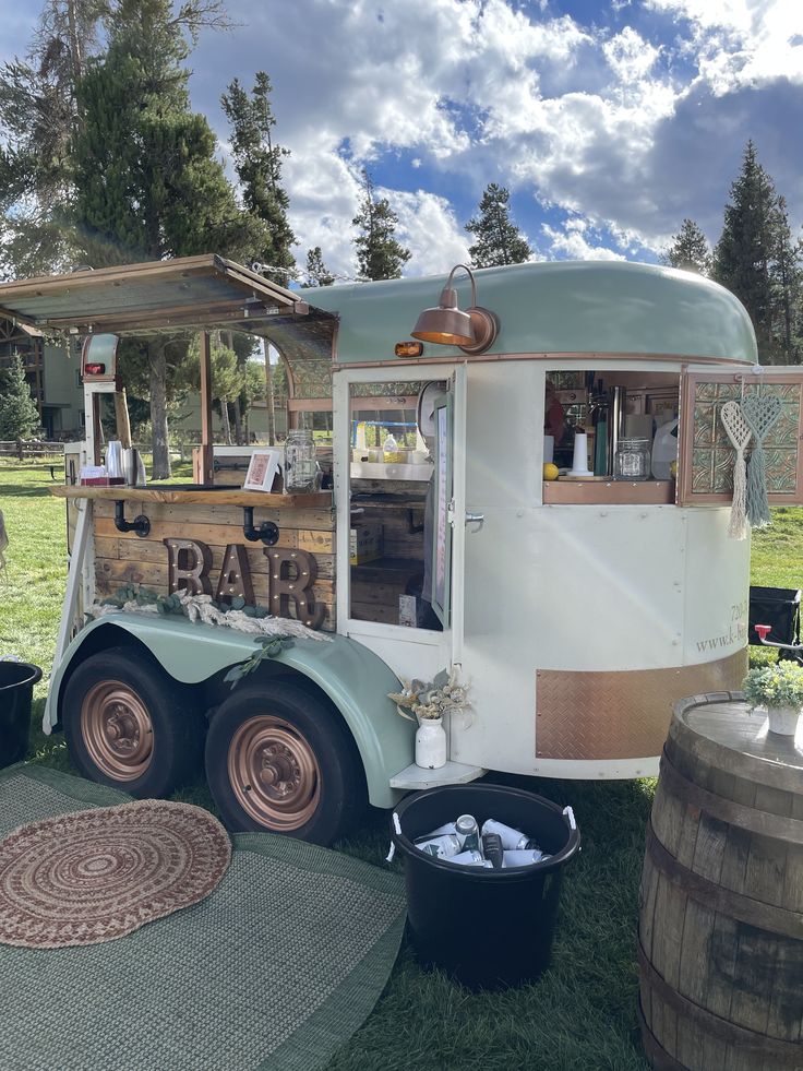 an old fashioned food truck is parked on the grass near some barrels and other items