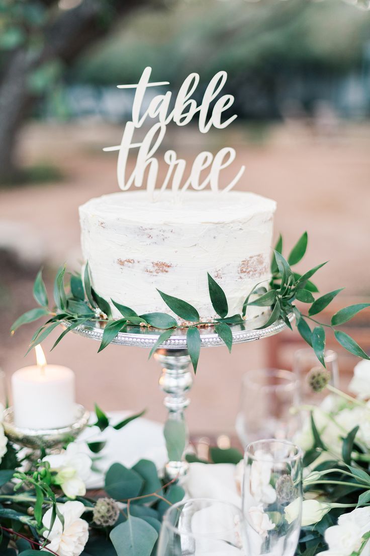 a table topped with a white cake covered in greenery