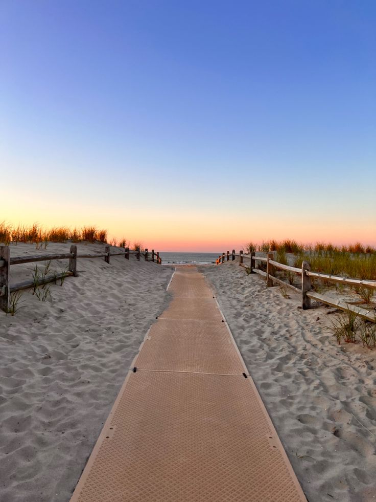 a wooden walkway leading to the beach at sunset