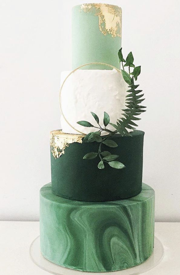 a three tiered green and gold wedding cake with greenery on the top layer