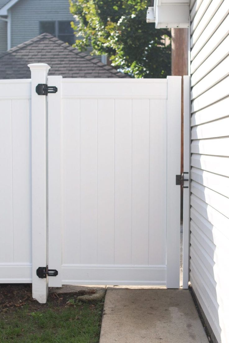 a white fence with two black handles on it and a house in the back ground