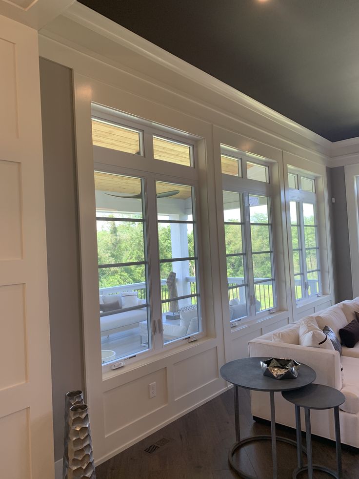 a living room with white couches and two tables in front of large windows that look out onto the street