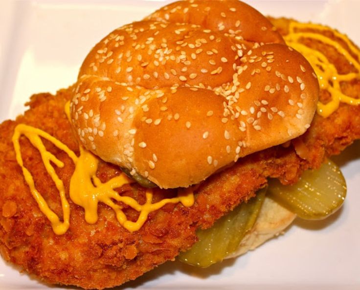 a fried chicken sandwich with pickles and cheese on a white plate, ready to be eaten