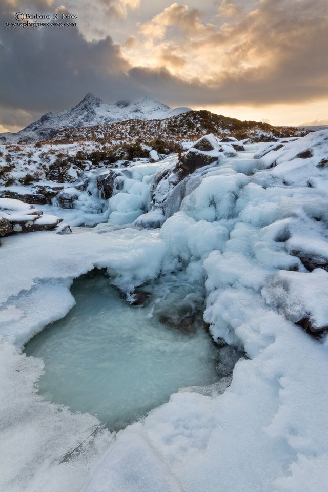 the water is frozen and there are mountains in the background with snow on it's sides