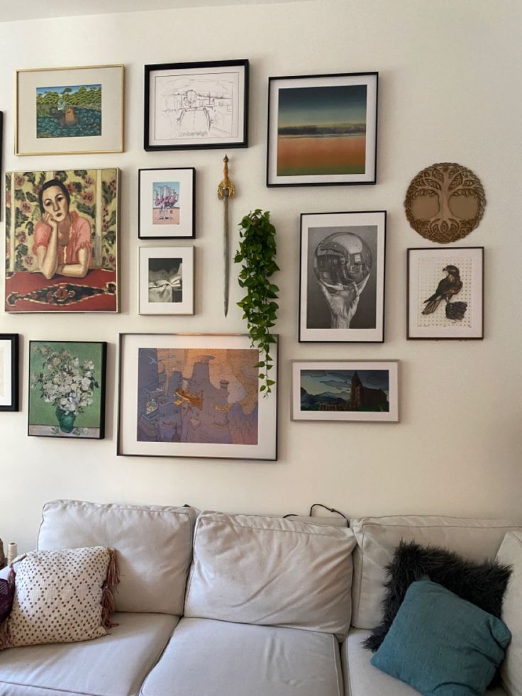 a white couch sitting in front of a wall covered with pictures and framed art on it