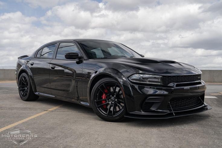 a black dodge charger parked in a parking lot with cloudy skies behind it and red rims on the tires