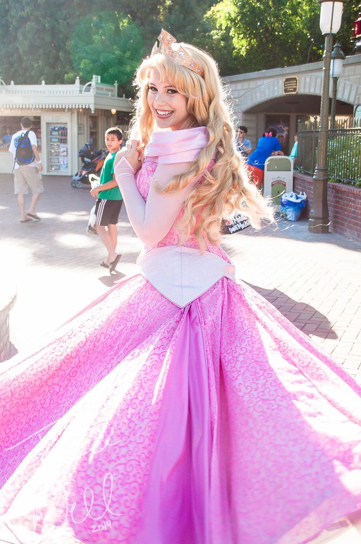 a woman in a pink and white dress posing for the camera with her long blonde hair