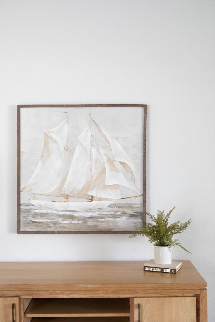 a painting hanging on the wall next to a wooden cabinet with a potted plant