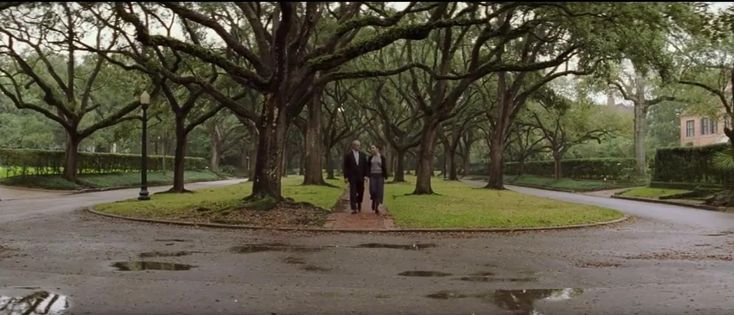 two men in suits are walking down the street with trees on either side of them