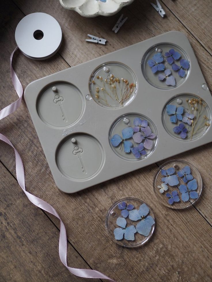 a muffin tin with blue and purple flowers in it on a wooden table next to ribbon