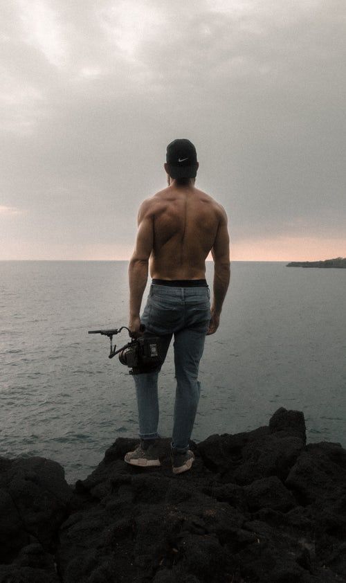 a man standing on top of a rocky cliff next to the ocean