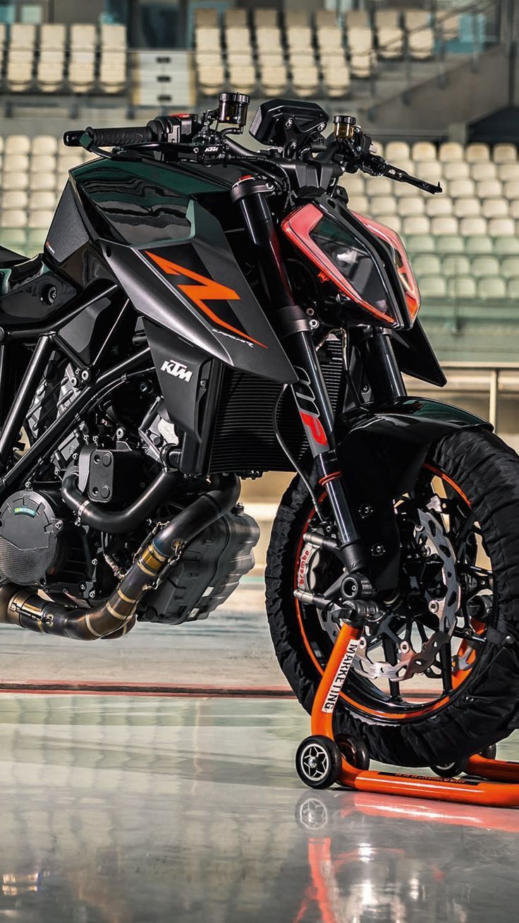 an orange and black motorcycle is parked in front of some bleachers with seats