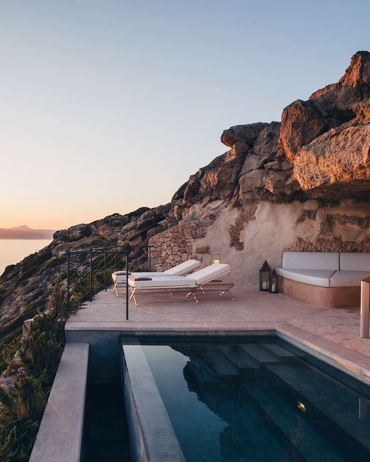 an outdoor swimming pool with chaise lounges next to the ocean at sunset or sunrise