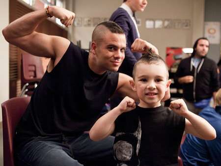 a man sitting next to a little boy with his arm in the air as he brushes his hair