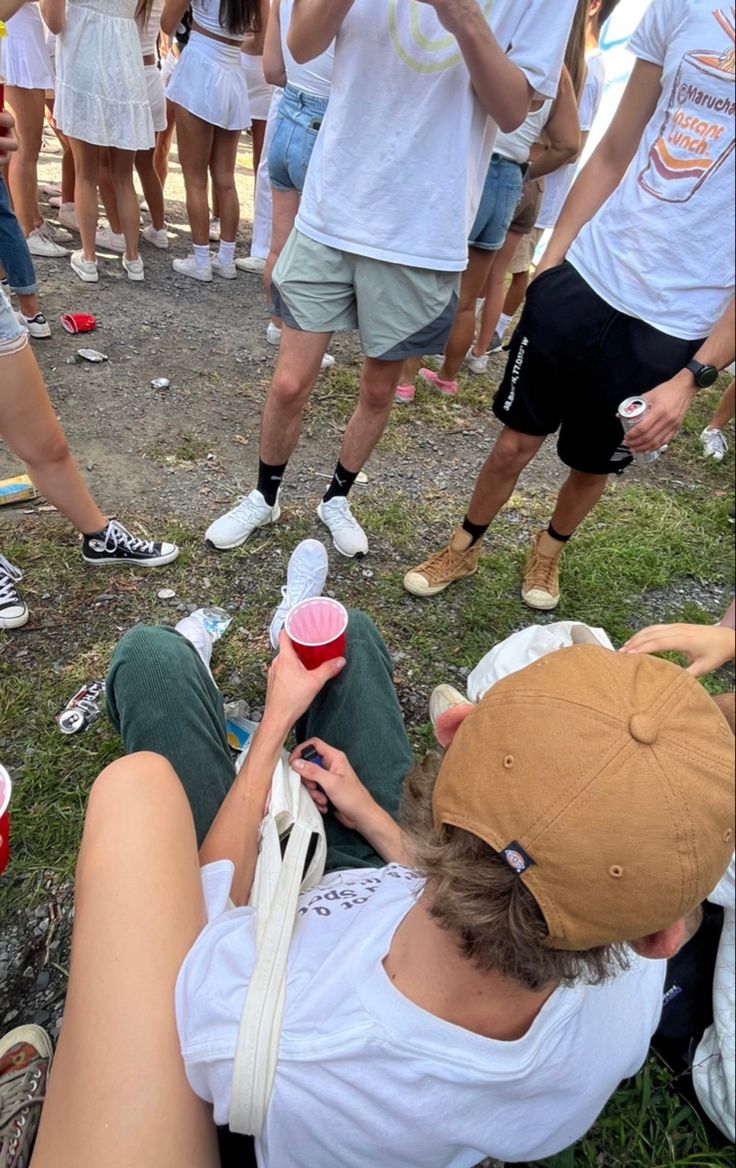 a group of people sitting on the ground with cups in their hands and one person holding a cell phone