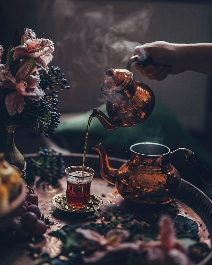 a person pouring tea into a cup on top of a tray with flowers and fruit