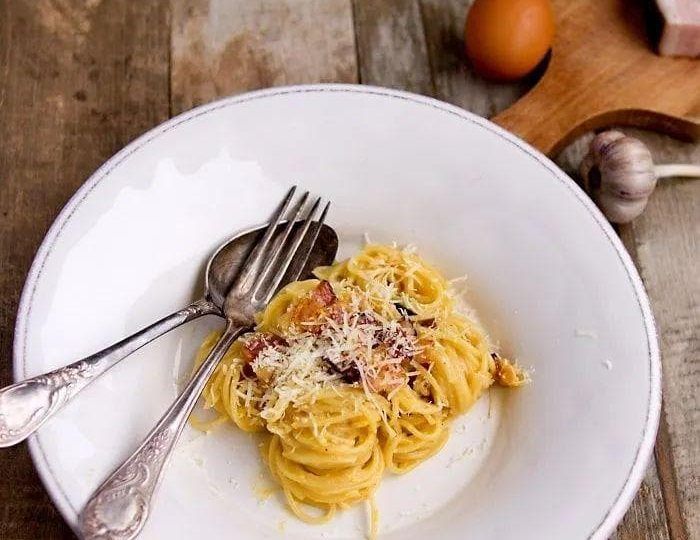 a white plate topped with pasta covered in sauce and parmesan cheese next to an egg