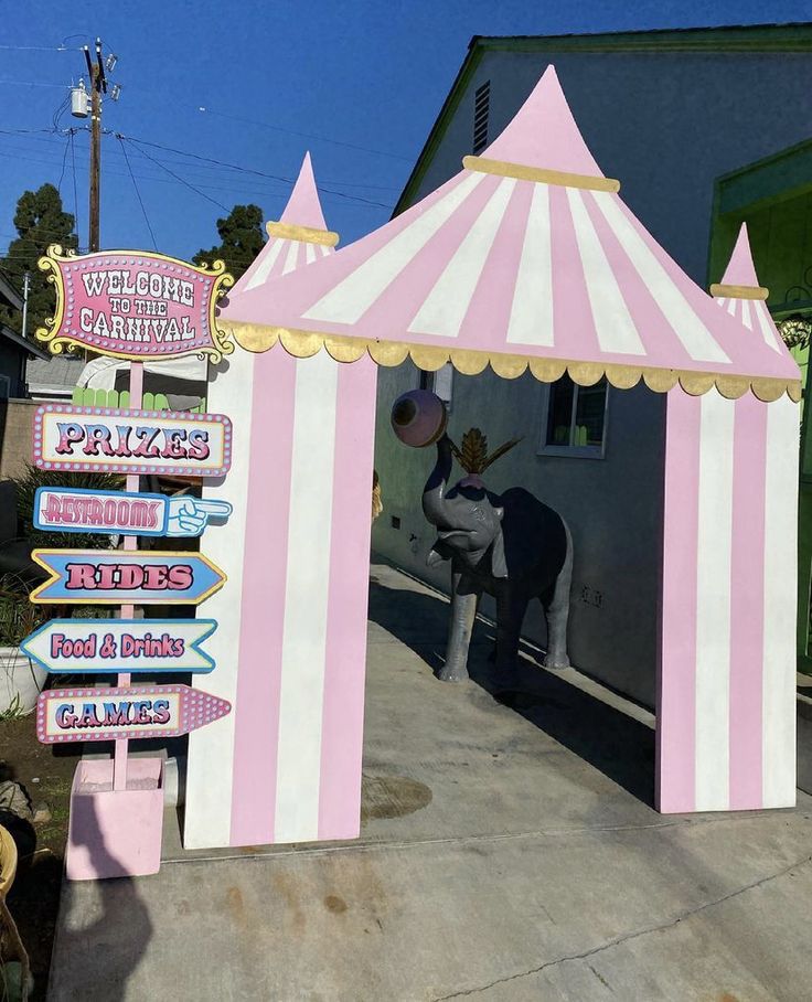 a pink and white circus tent sitting on the side of a road next to a sign