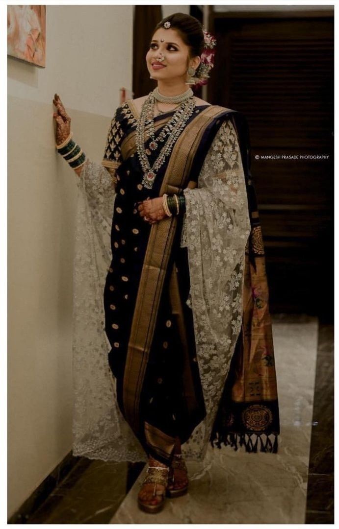 a woman in a black and white sari standing next to a wall with her hand on