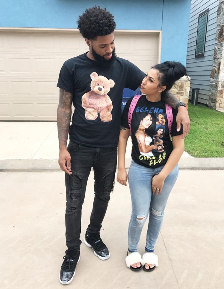 a young man and woman standing in front of a garage with a teddy bear t - shirt on