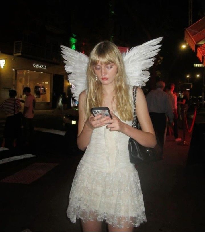 a woman dressed as an angel holding a cell phone in her hand and looking at the screen