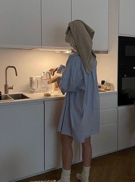 a person in a robe is standing at the kitchen counter and looking into the oven