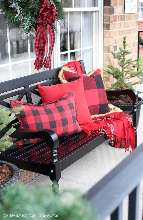 a black bench with red and black pillows sitting on it's side next to a christmas tree