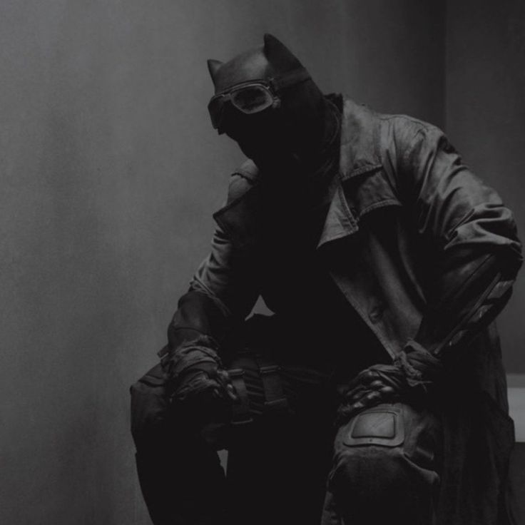 black and white photograph of a man in a batman costume sitting on a toilet seat