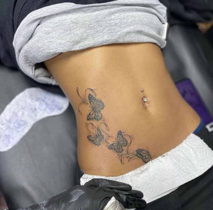 a woman's stomach with butterfly tattoos on her lower back and the bottom part of her abdomen