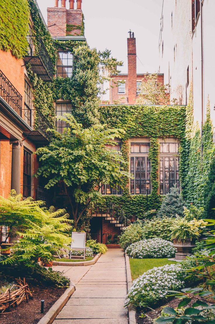 an alley way with lots of plants and trees on both sides, surrounded by brick buildings