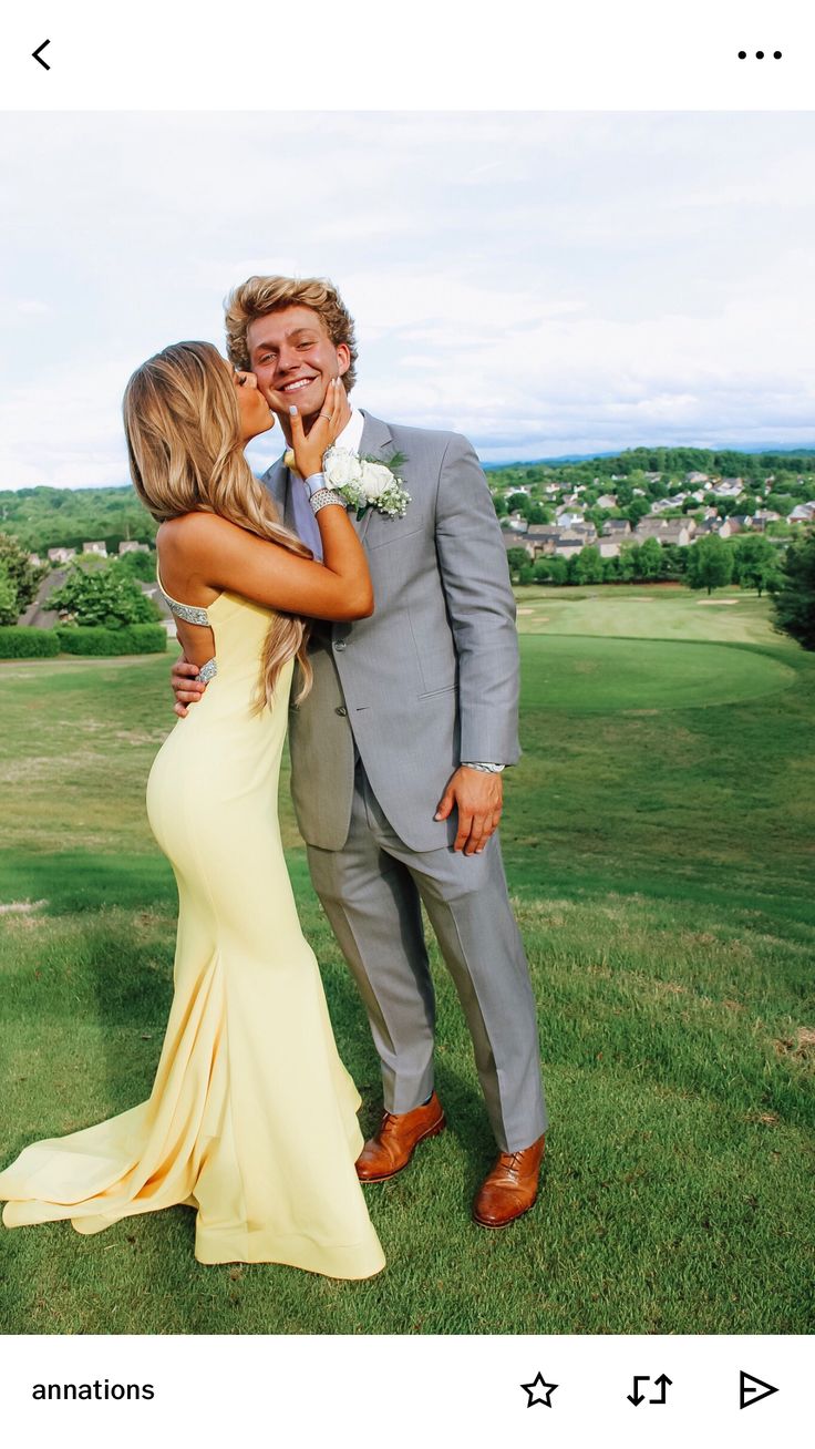 a man in a suit and woman in a yellow dress hugging each other on the grass