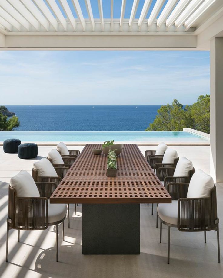 an outdoor dining table and chairs with the ocean in the background