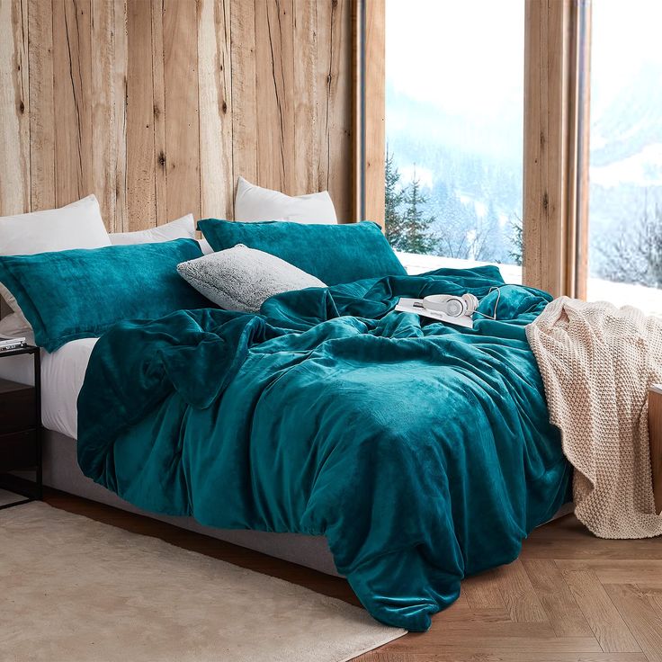 a bed with teal comforter and pillows in a bedroom next to a window