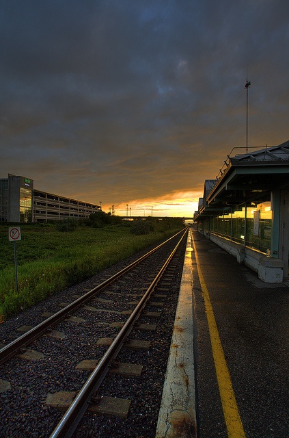 an empty train station at dusk with the sun setting behind it and dark clouds in the sky