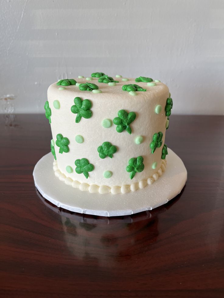 a white cake with green frosting and shamrocks on it sitting on a wooden table