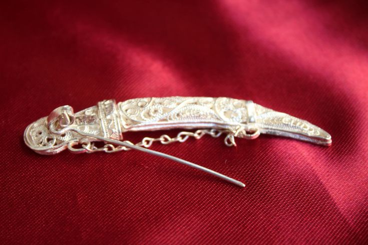 Filigree jewelry silverwork has been a long tradition in the city of Shkoder, Albania. This jewelry is handcrafted using silver, which is one of the only precious metals that allow for this delicate form of artwork. Specific details on this product: Dimensions: 7cm x 1cm Net Weight: 10gr The mini-sword can be removed from the sheath but the chain length prevents it from doing so entirely. Remove the chain and you can freely remove the whole sword from the sheath. It's a creative piece of jewelry and definitely impressive. Traditional Ceremonial Brooch Jewelry, Traditional Formal Brooch With Intricate Design, Traditional Silver Brooches For Formal Occasions, Traditional Handmade Sterling Silver Brooches, Traditional Handmade Brooch For Formal Occasions, Handmade Traditional Brooch For Formal Occasions, Traditional Silver Filigree Brooch, Victorian Silver Brooches For Ceremonial Use, Victorian Silver Brooches For Ceremonial Occasions