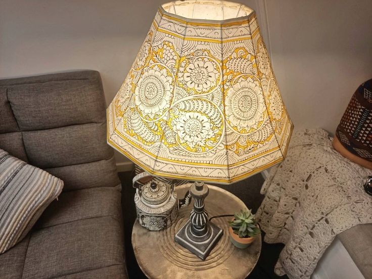 a lamp sitting on top of a metal table next to a gray couch and pillows